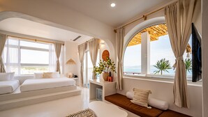 A modern bedroom with a large bed, a seating area, and a view of the sea. - Happiness Hotel (Quy Nhon Dong)