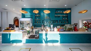 Eine moderne Bar mit Türkis-Farben, hängenden Korbschwingenlampen und einer Auswahl an Flaschen und Gläsern in Regalen.