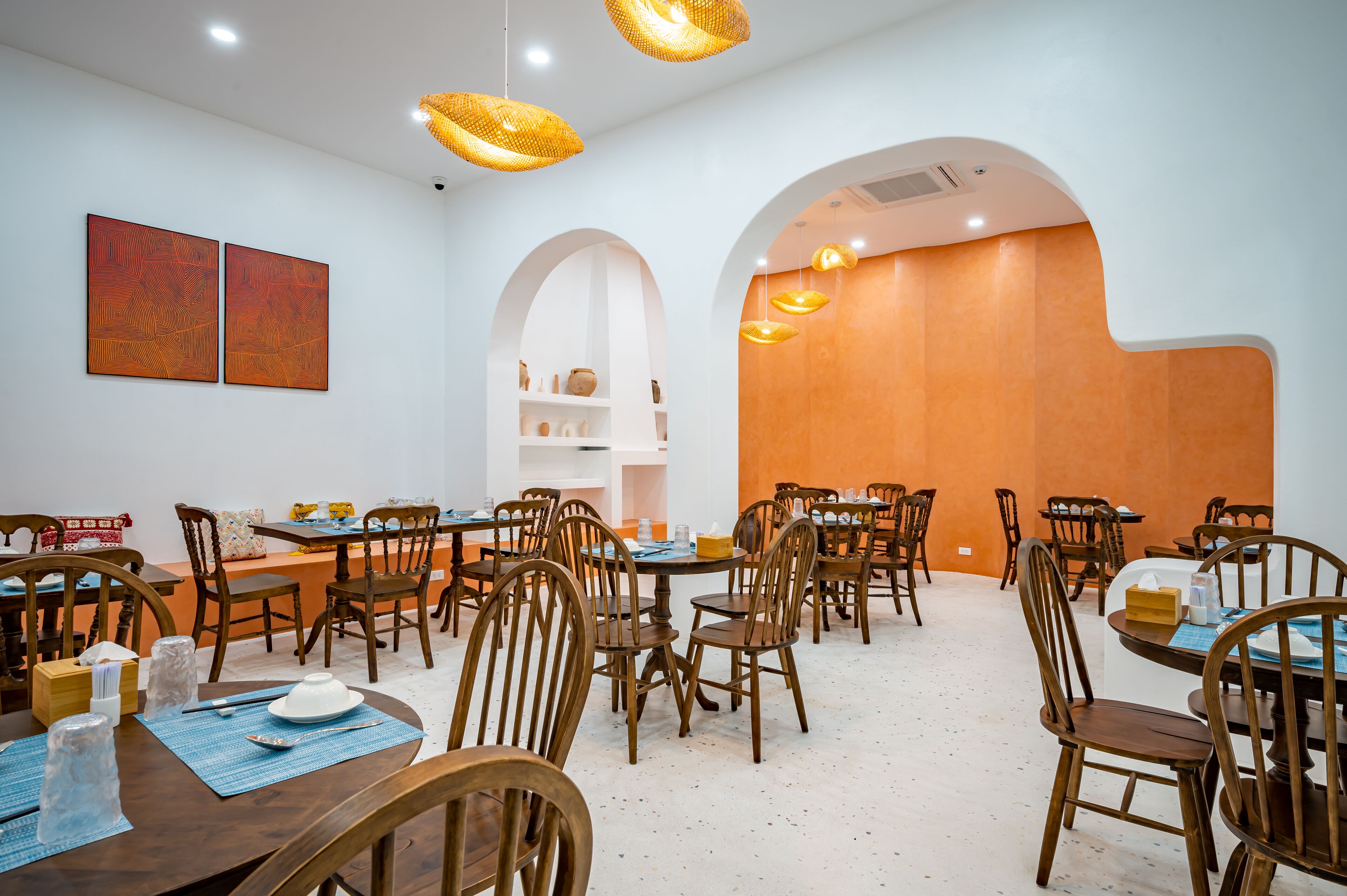 A dining area with wooden tables and chairs, white walls, and a wooden accent wall.