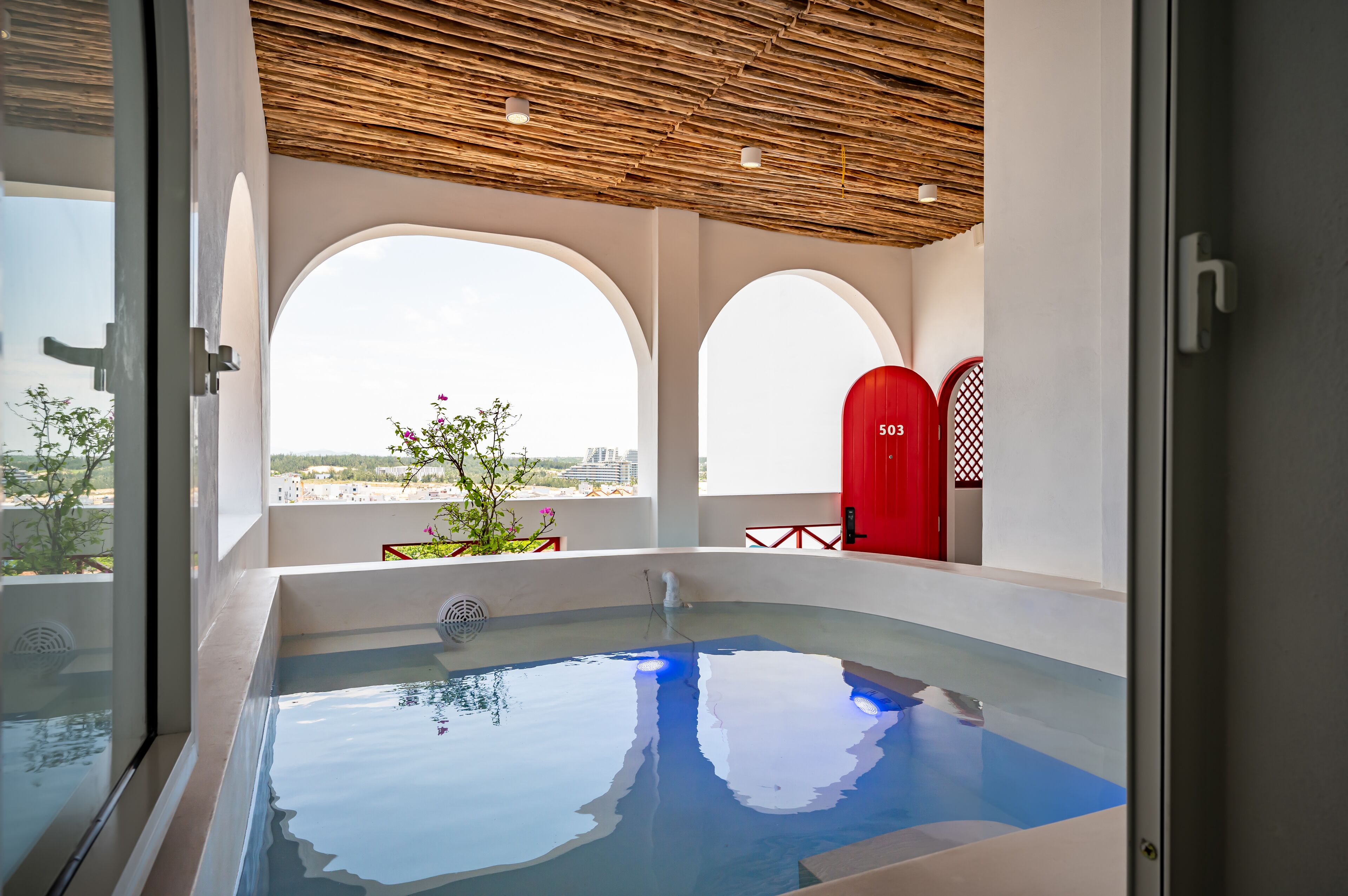 Une piscine intérieure moderne, dotée d’une eau cristalline, de grandes fenêtres en arc de cercle et offrant une vue sur le paysage urbain.