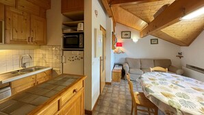 A compact kitchen with wooden cabinets, a microwave, and a refrigerator. There is a dining area with a table and chairs, and a sofa. - Ski-in/Ski-out, Sleeps 6, 3 Rooms, Balcony, Parking, Crest-Voland (Crest-Voland)