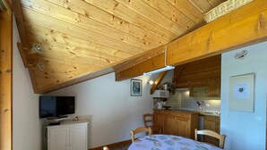 A cozy attic bedroom with a wooden ceiling, a TV, a bed with a tropical print bedspread, and a kitchenette with wooden cabinets. - Ski-in/Ski-out, Sleeps 6, 3 Rooms, Balcony, Parking, Crest-Voland (Crest-Voland)
