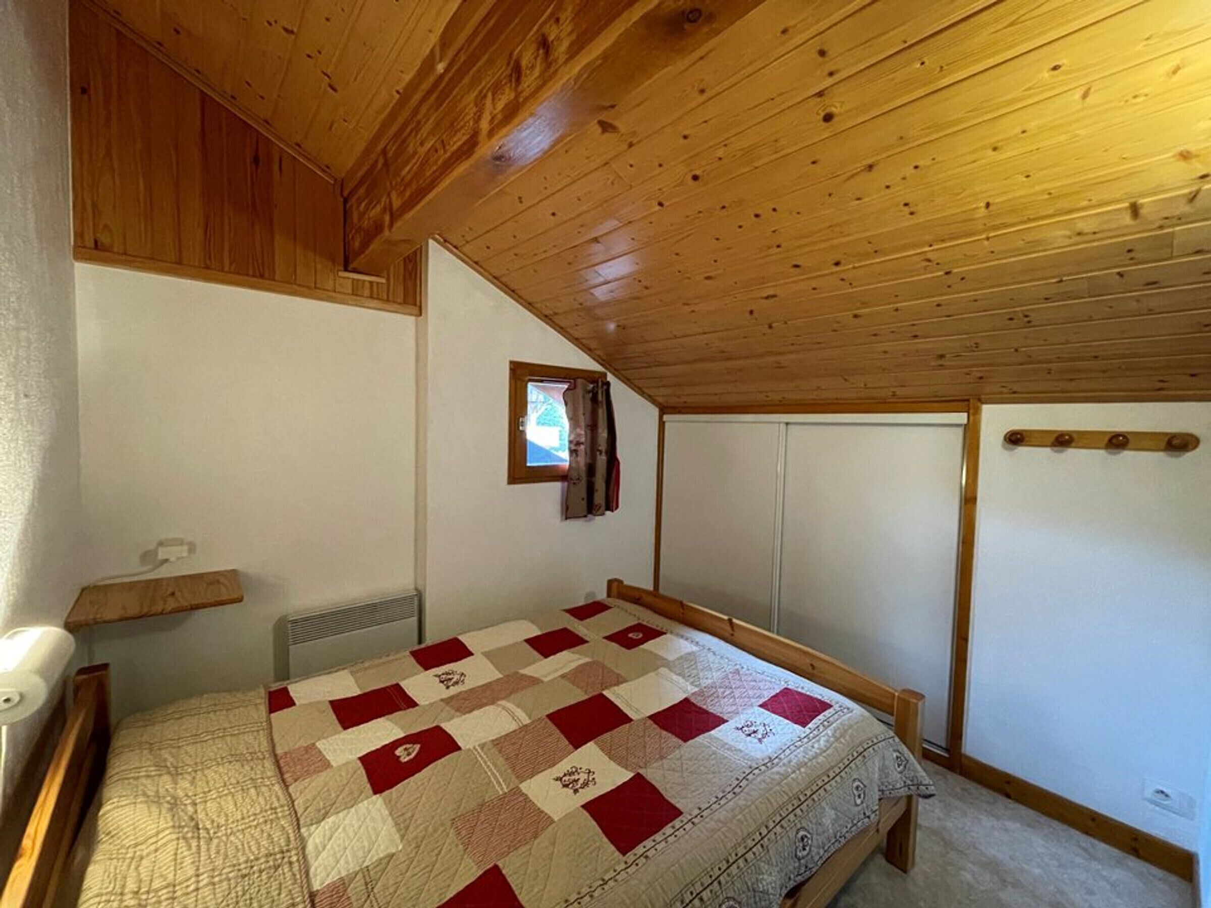 Una camera da letto con soffitto in legno, copriletto trapuntato, una piccola finestra e un riscaldatore a parete.