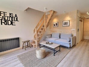 Un salon moderne avec un escalier en bois, un canapé gris, une petite table et un radiateur.