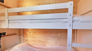 Una cama litera con ropa de cama blanca en una habitación con paredes de madera y techo inclinado.