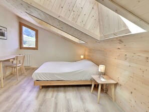 A bedroom with a wooden ceiling, a bed, a desk, a chair, and a window.