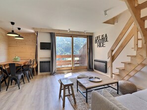 Un intérieur moderne comprenant un coin repas, un canapé, une table basse, un escalier et une vue dégagée sur l’extérieur grâce à une grande fenêtre.