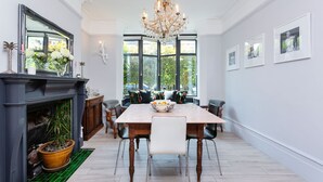 Ein Esszimmer mit großem Tisch, Stühlen, einer Chandelierleuchtre, einem Kamin und Blick durch große Fenster.