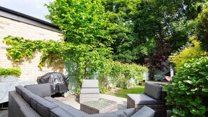 Eine Terrasse mit einer grauen Couch, zwei Sesseln und einem kleinen Tisch.