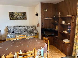 Un accogliente soggiorno con un divano decorato, una televisione e un mobiletto in legno con ripiani.