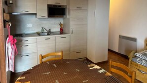 Cocina compacta con microondas, pileta y alacenas de madera. Se observa una mesa de comedor con un mantel individual y sillas.