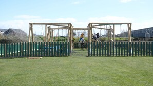 Une aire de jeux avec des balançoires et un espace délimité par une clôture.