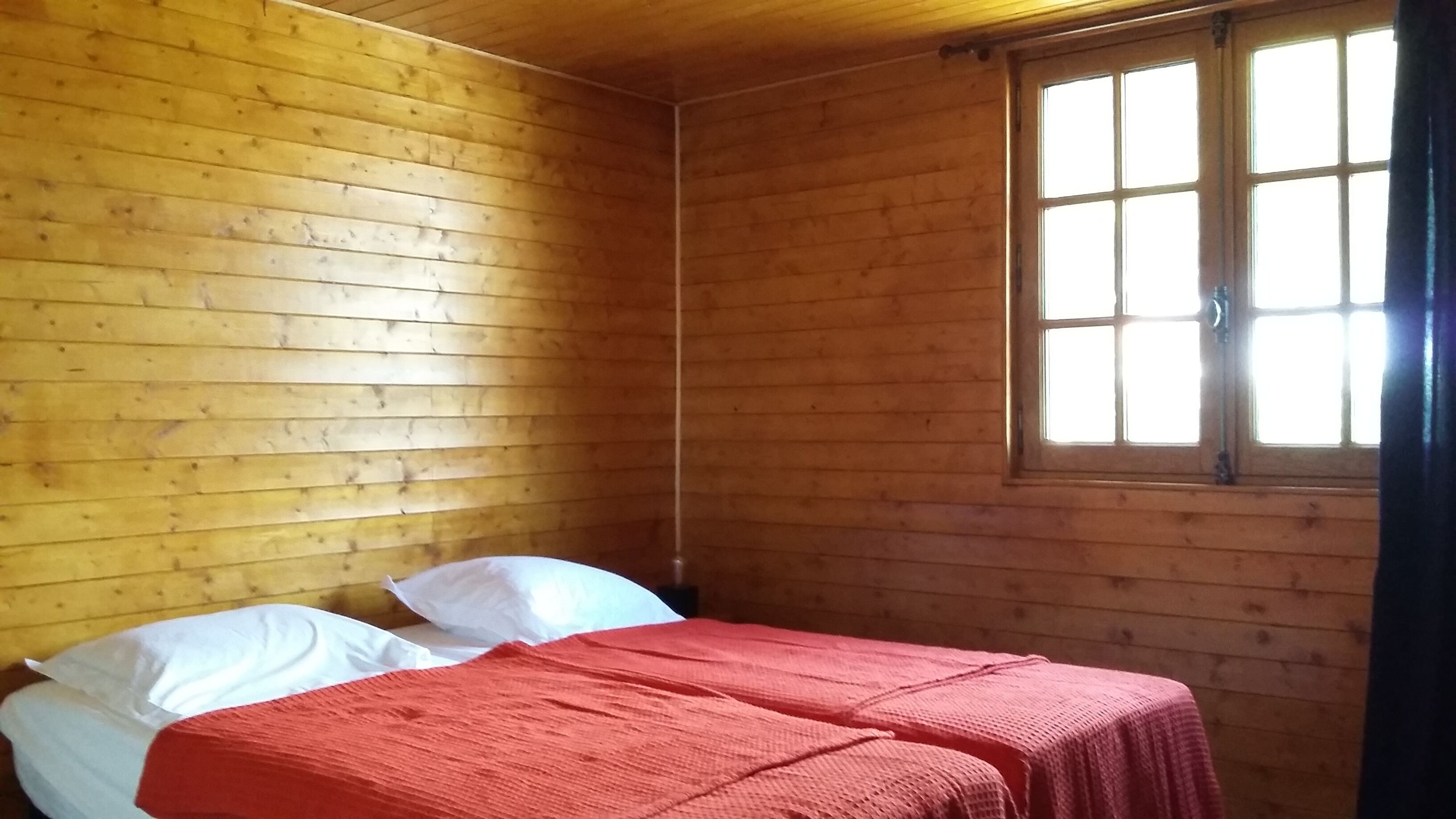 Une pièce de cabane en bois avec deux lits, une fenêtre et un plafond en bois.