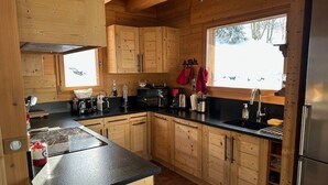 A cabin-style kitchen with wooden cabinets, a black countertop, and a stainless steel refrigerator.