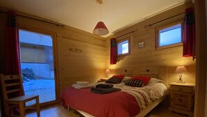 A wooden cabin bedroom with a bed, two bedside tables, a chair, and a window.
