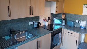 A modern kitchen with wooden cabinets, a stainless steel sink, a kettle, a toaster, and a microwave. - Apartment - Sleeps 5, Sun Terrace (Skegness)