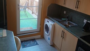 A compact kitchen with a washing machine, a sink, and a door leading to a fenced outdoor area. - Apartment - Sleeps 5, Sun Terrace (Skegness)