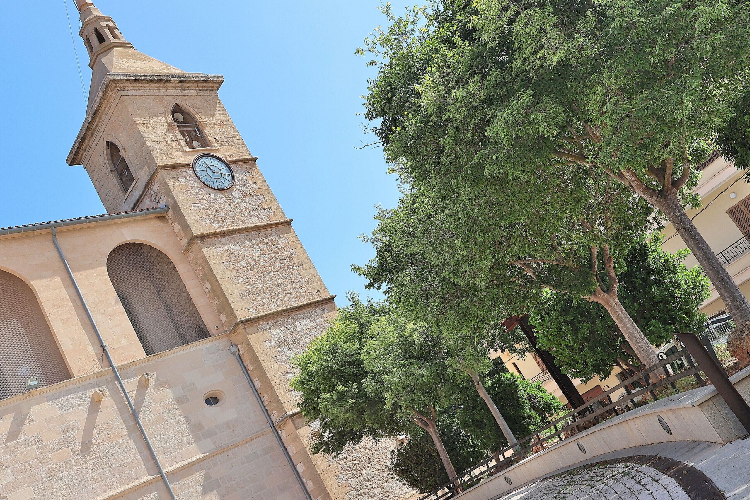A historic building with a clock tower, stone arches, and a tree-lined courtyard.