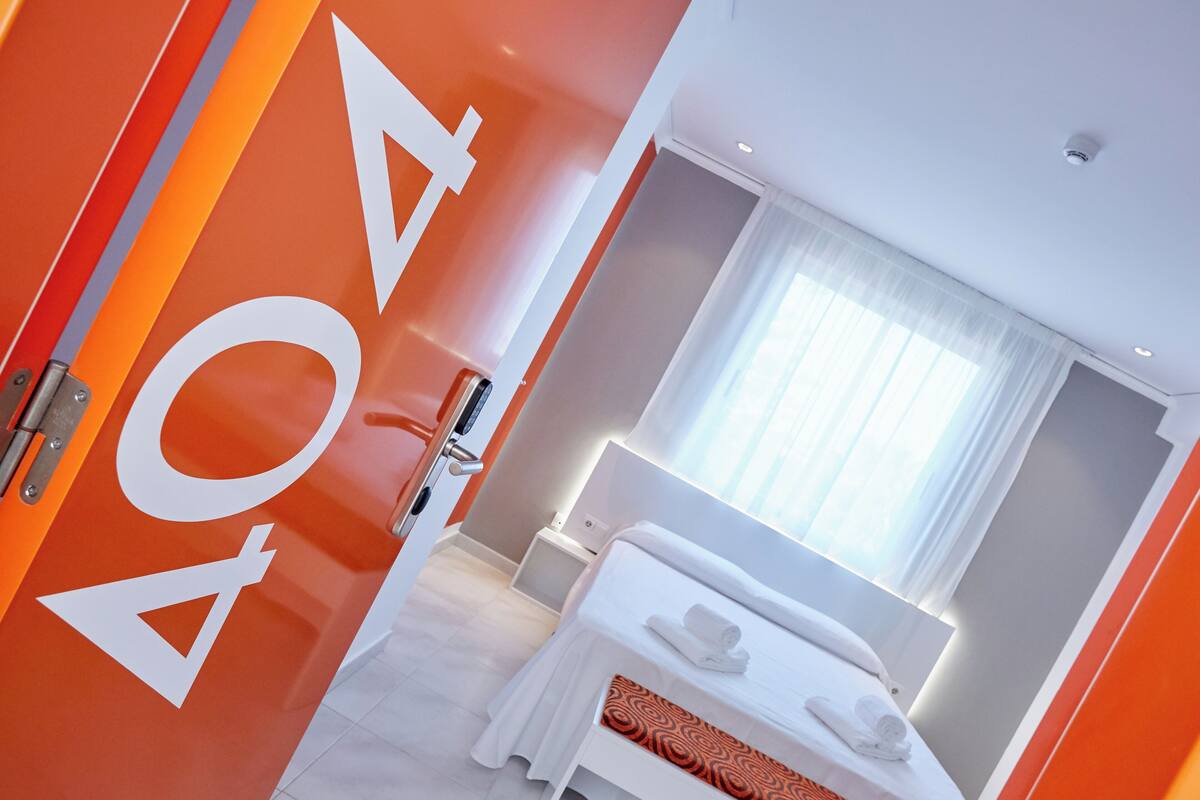 Una habitación de hotel moderna con una cama grande, una mesita de noche y una ventana con cortinas.