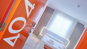 Une chambre d’hôtel moderne avec un grand lit, une table de chevet, une commode et une fenêtre avec des rideaux.