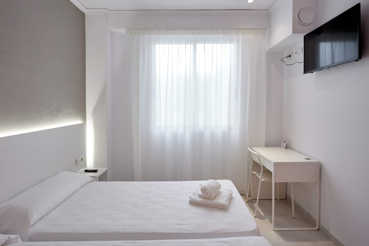 Una habitación de hotel moderna con una cama bien hecha, un escritorio y un televisor montado en la pared.