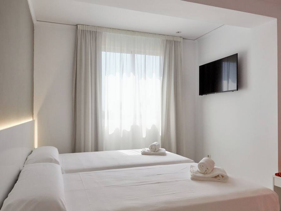 Camera d'albergo con un letto, una TV a parete e una finestra con tende.