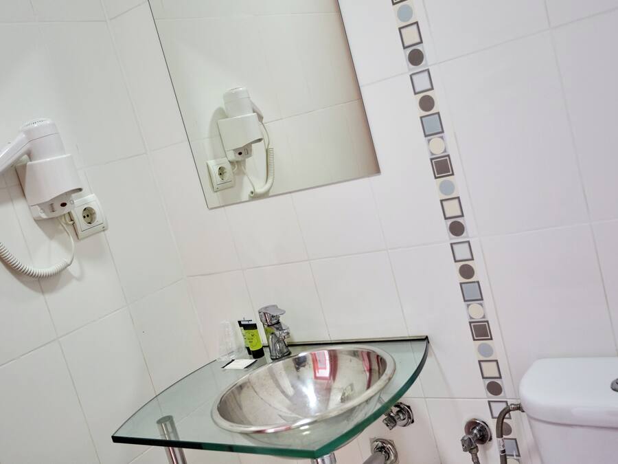 A bathroom with a glass sink, a white toilet, and a wall-mounted hairdryer.