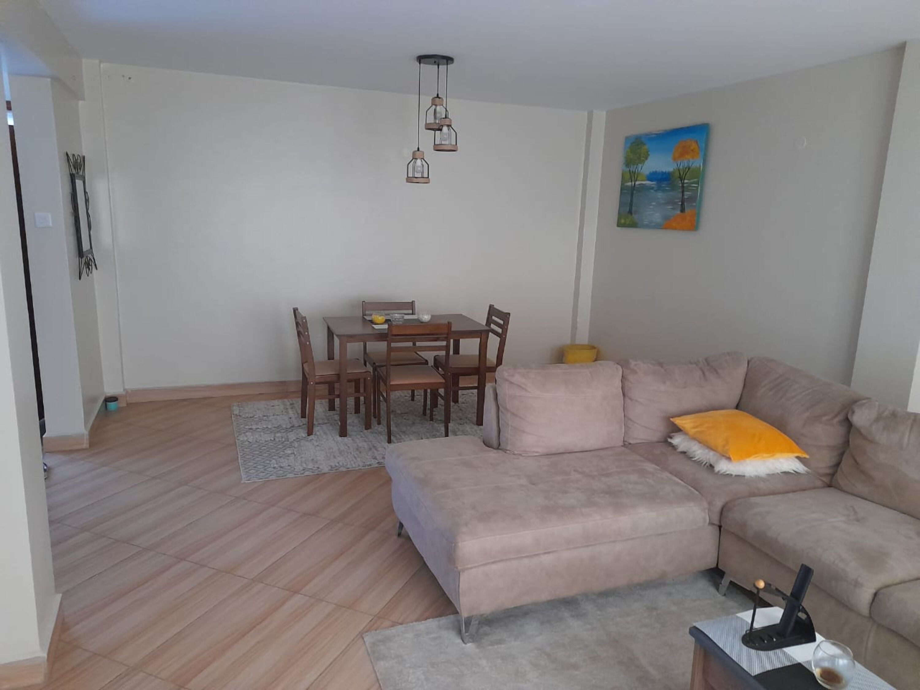 Un salon avec un canapé beige, une table à manger entourée de chaises et un tableau accroché au mur.