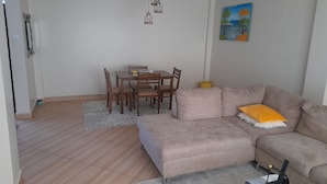 A living room with a beige sofa, a dining table with chairs, and a painting on the wall. - Affordable Heaven by CHH (Nairobi)