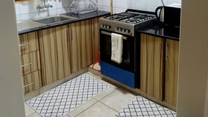 A compact kitchen with a gas stove, a sink, and wooden cabinets. - Affordable Heaven by CHH (Nairobi)