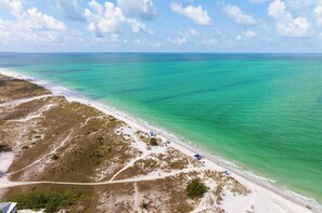 Een strand met helder turquoise water, een zandstrand en enkele mensen.