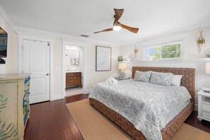 A bedroom with a large bed, a ceiling fan, a nightstand, a dresser, and a window with blinds.