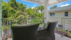 Área externa coberta com móveis de vime e vista para vegetação exuberante e uma casa ao fundo.