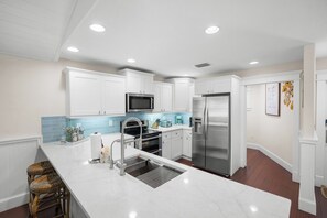 A modern kitchen with white cabinetry, stainless steel appliances, and a marble countertop.