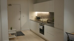 A compact kitchen with white cabinets, a built-in oven, and a countertop with a kettle and a dish rack. - Stunning 1-bed Apartment in London (London)