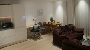A modern living room with a brown sofa, a dining table with chairs, a small kitchen area with a microwave, and a potted plant. - Stunning 1-bed Apartment in London (London)