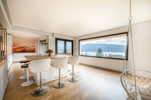 Enjoy a panoramic mountain view from the comfort of this room, featuring a dining table, bar stools, and a cozy hanging chair.