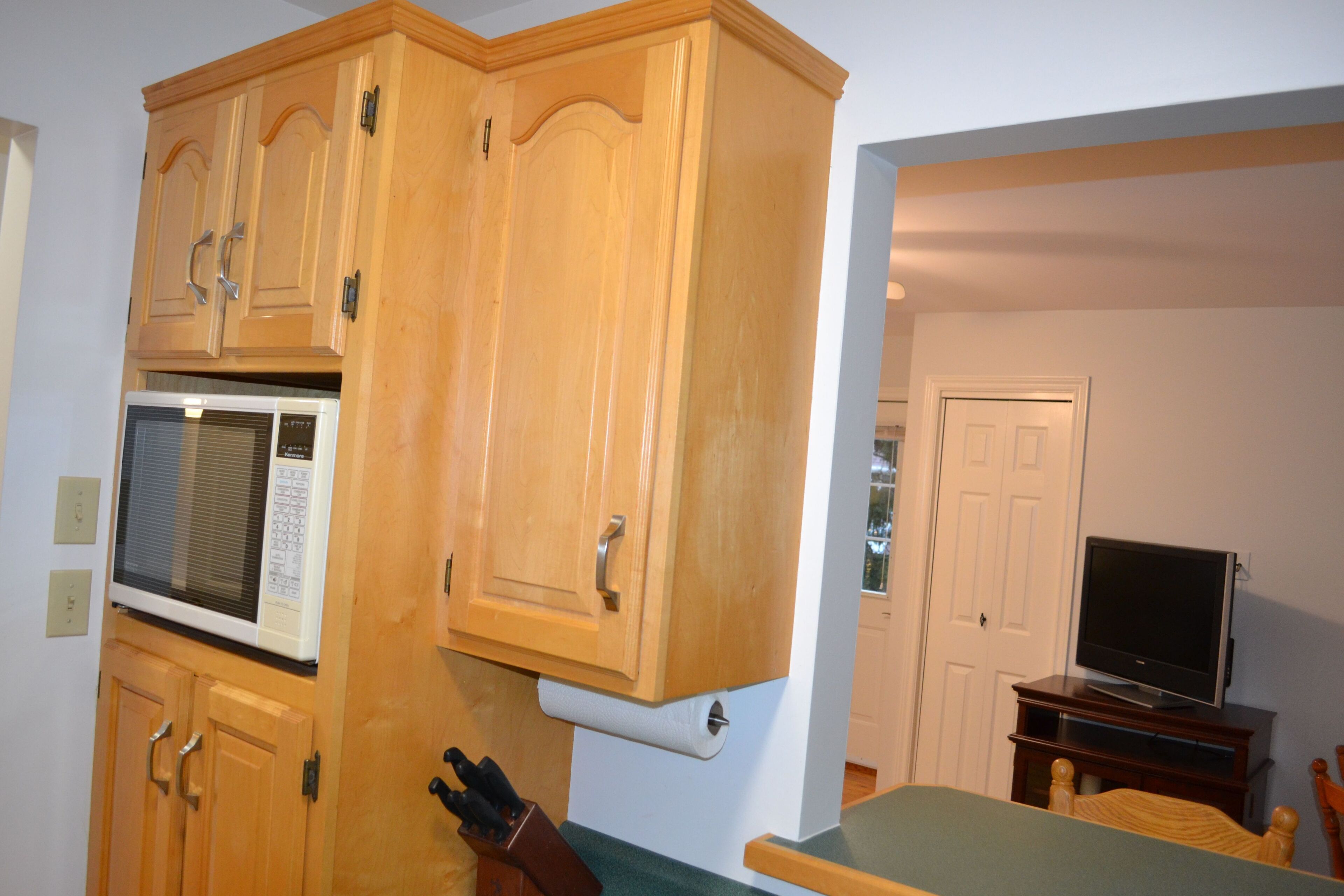 Una cocina con armarios de madera, un microondas y un televisor.