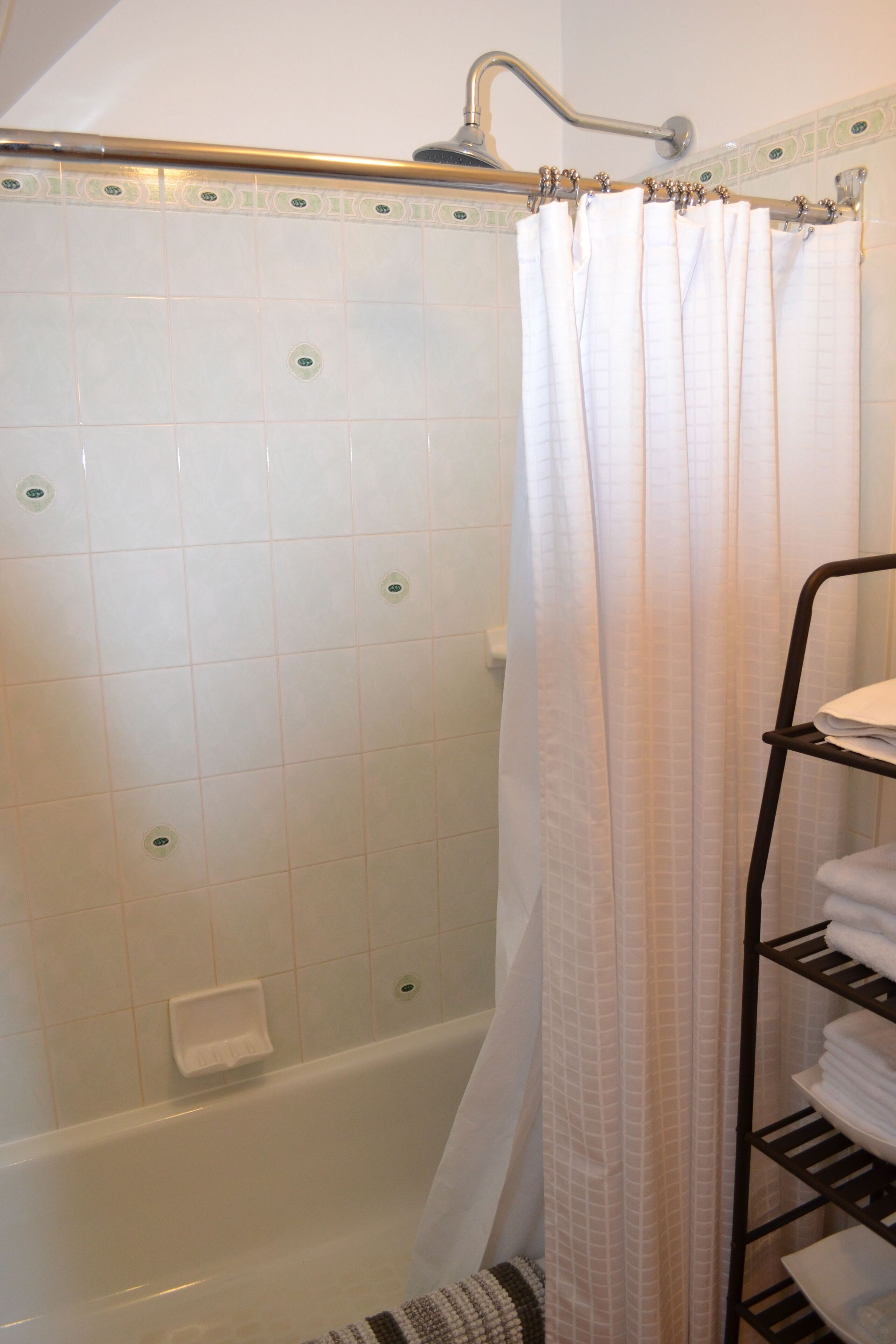 A bathroom with a bathtub, a shower curtain, and a towel rack with folded towels.