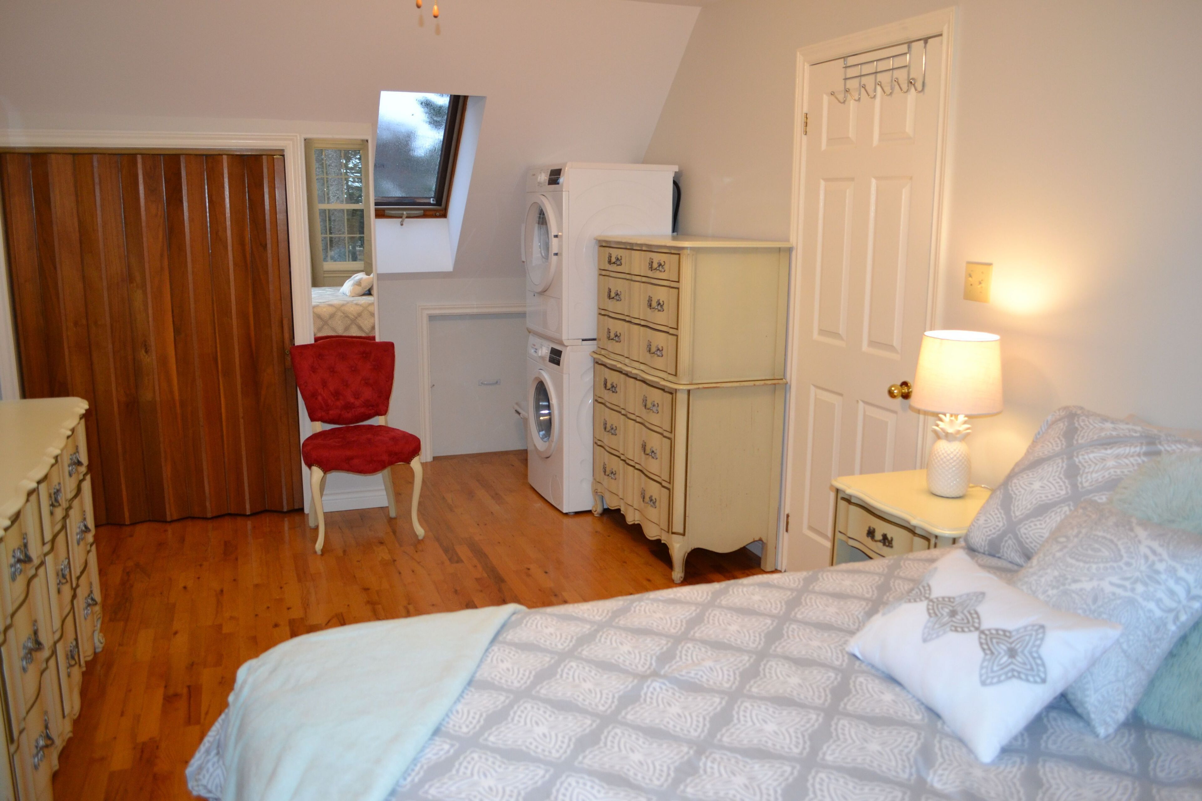 A bedroom with a bed, a chair, a dresser, a washing machine, and a television mounted on the wall.