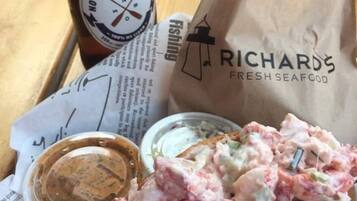 Ein Sandwich mit Soße, eine Bierflasche und eine Papiertüte mit Meeresfrüchte-Logo auf einem Holztisch.