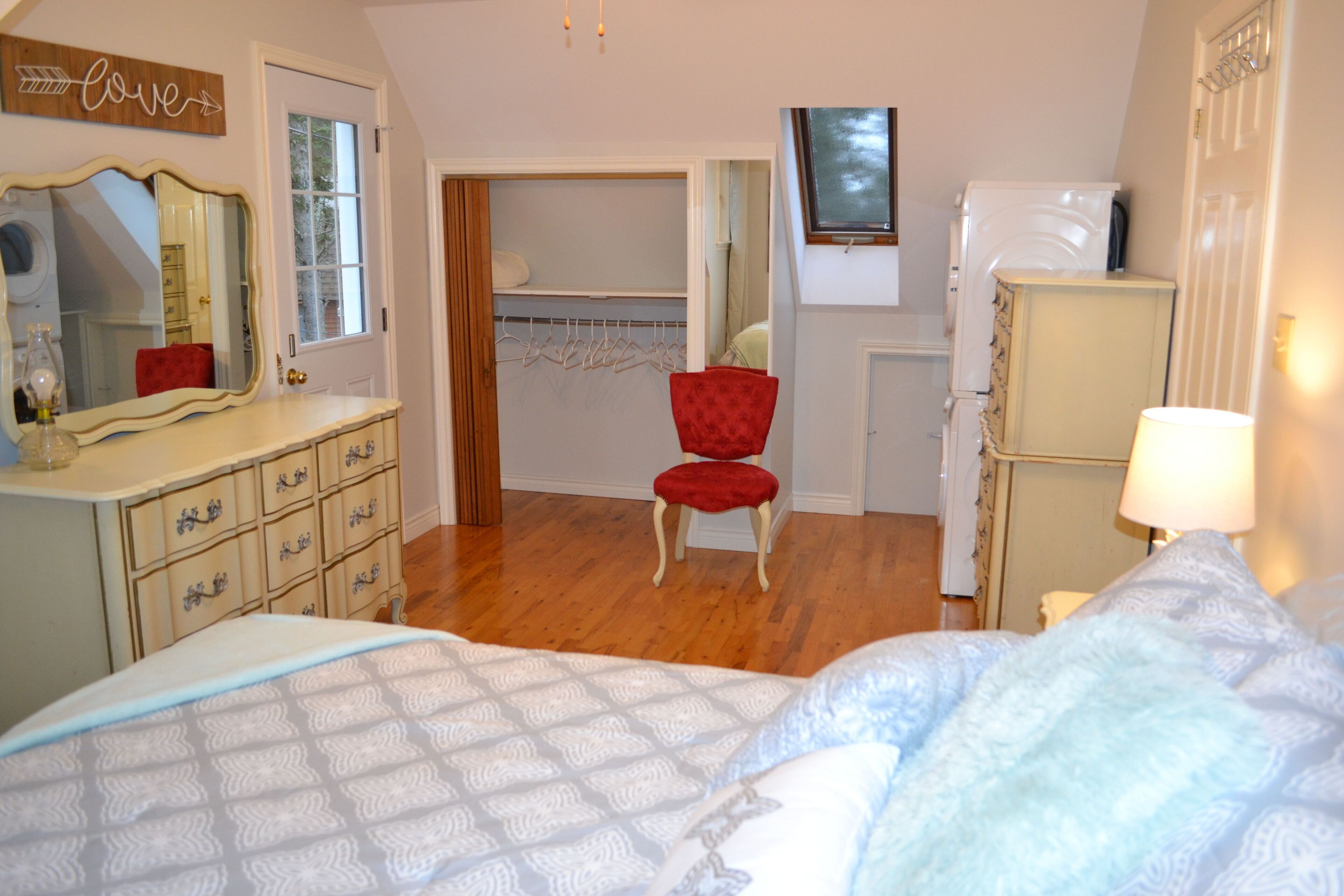 Une chambre à coucher avec un lit, une commode, un miroir, un placard et une chaise rouge.