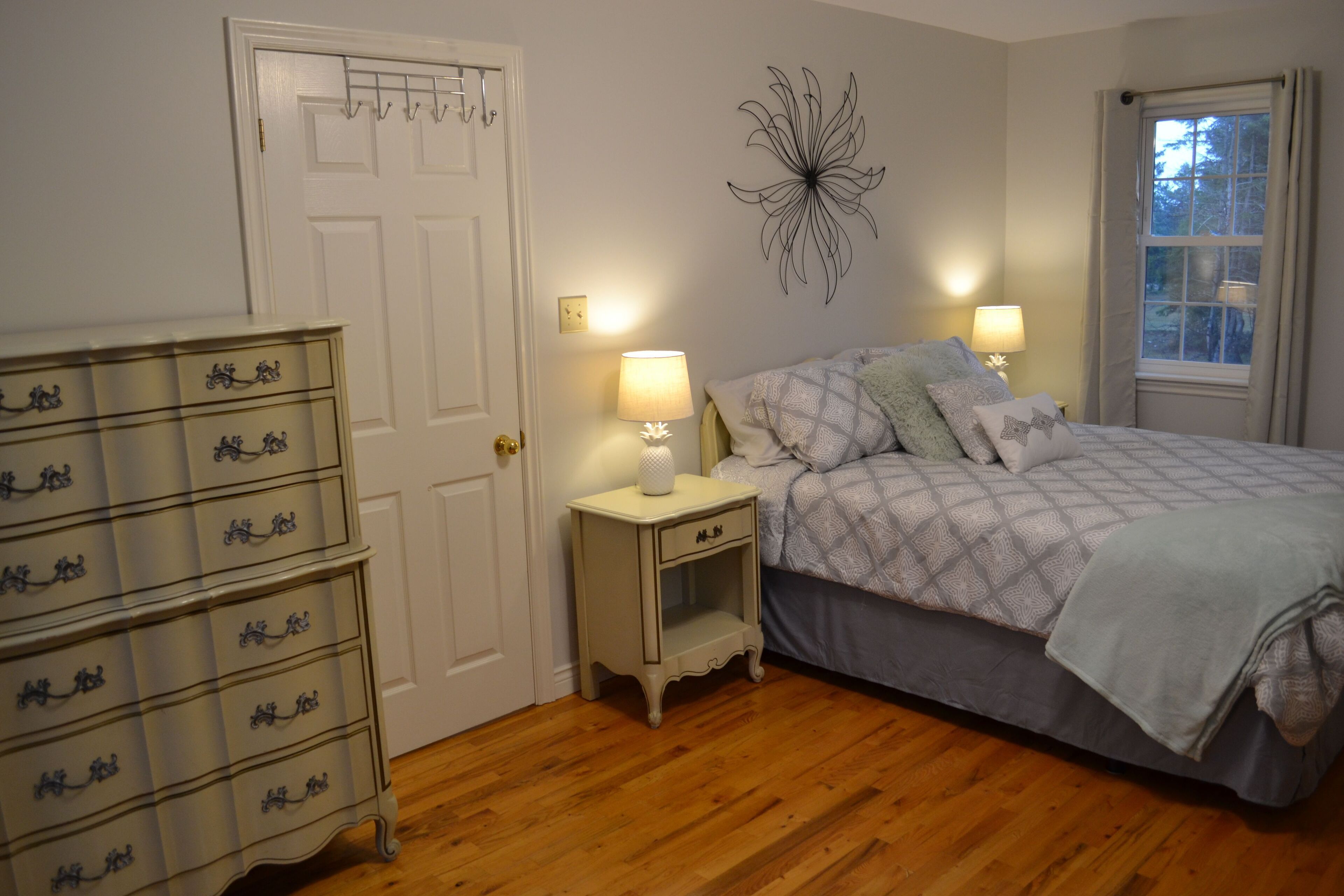 Un dormitorio con cama, lámparas de noche, cómoda y un adorno en la pared.