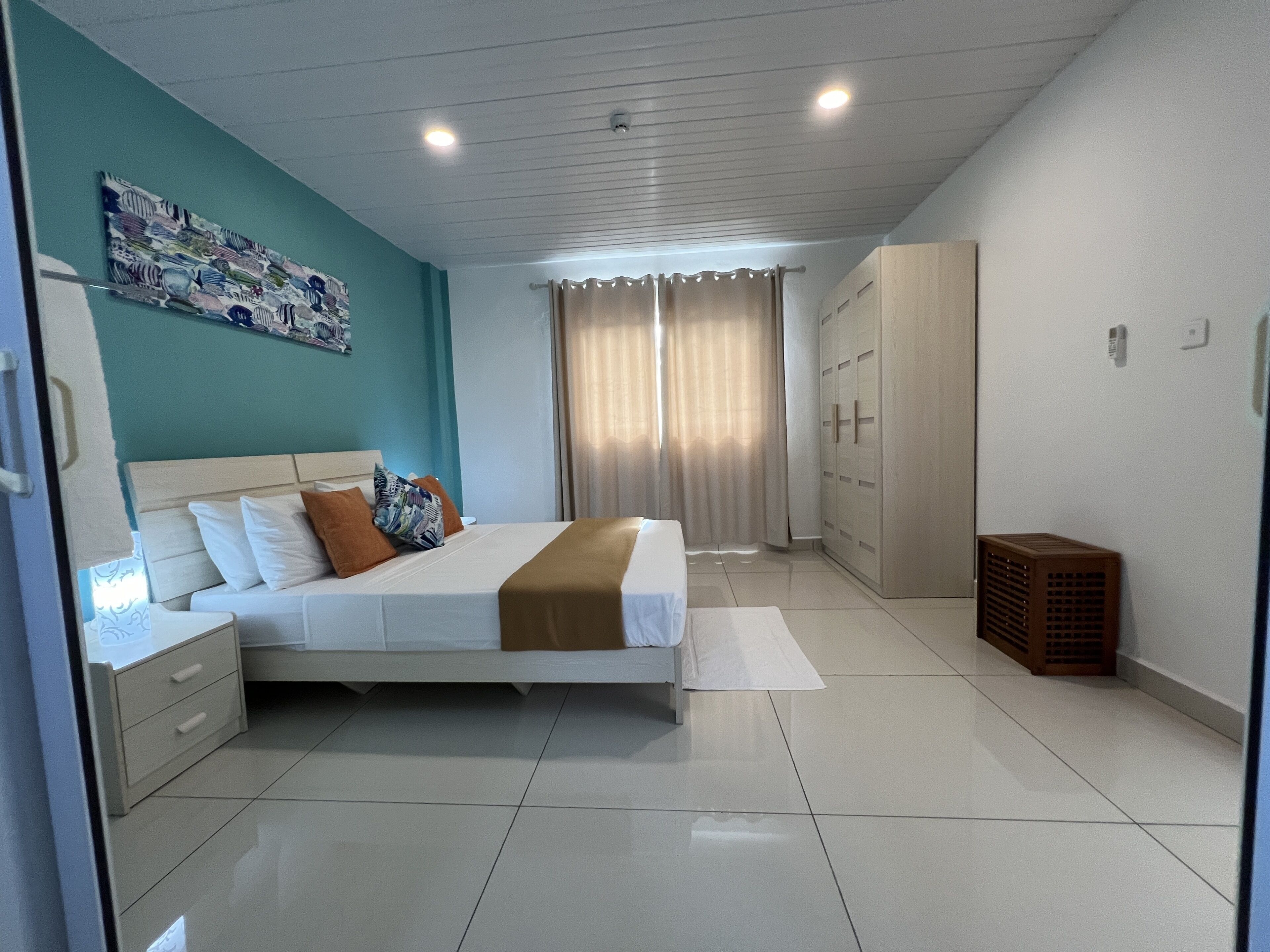 A modern bedroom with a bed, bedside tables, a wardrobe, and a large window with curtains.