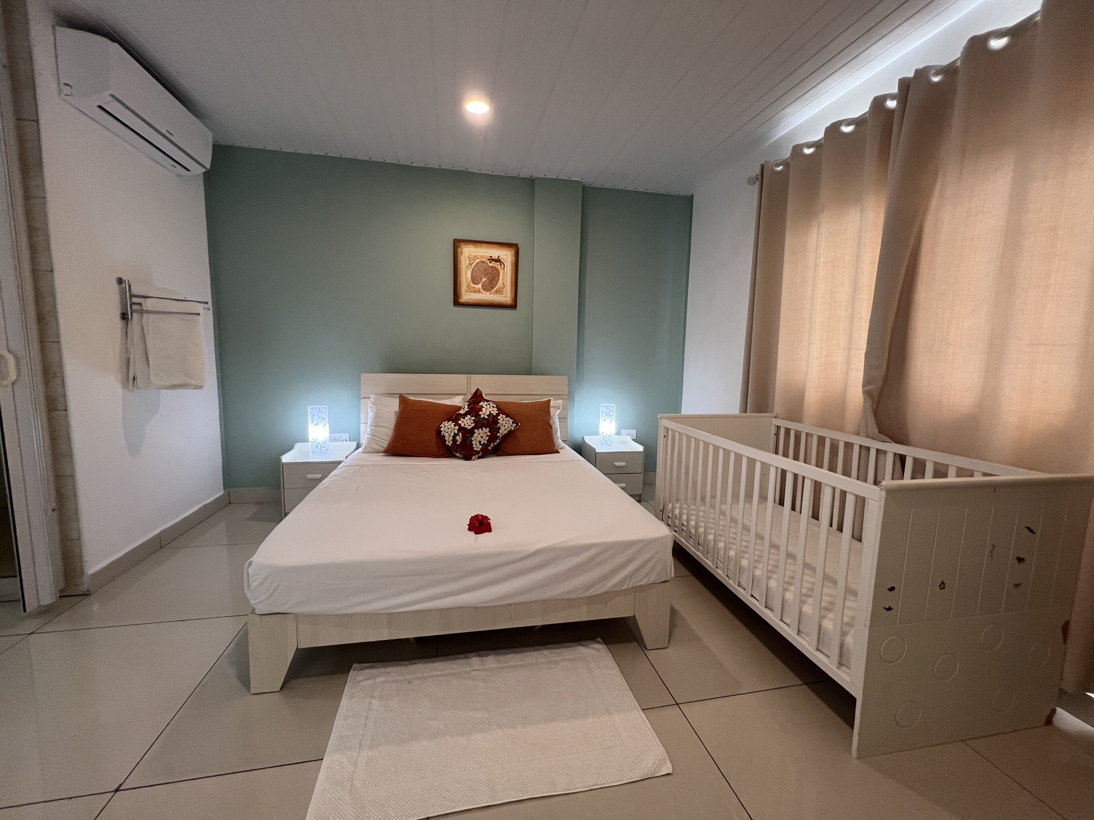 Een slaapkamer met een bed, een ledikant, een nachtkastje, een wandairconditioner en een lijst met een foto aan de muur.