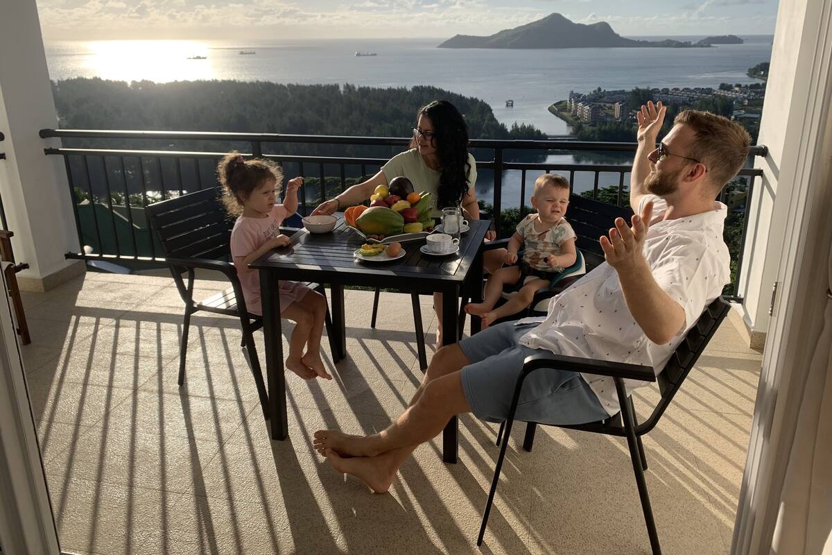 Un balcón con una mesa dispuesta para una comida, con vistas a un paisaje marino y una isla distante.