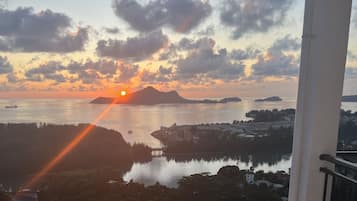 Vista do pôr do sol a partir de uma varanda com vista para águas calmas, ilhas distantes e uma ponte.