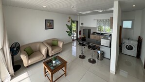 Una sala de estar moderna con un sofá color crema, una mesa de centro de vidrio y una cocina con lavadora.