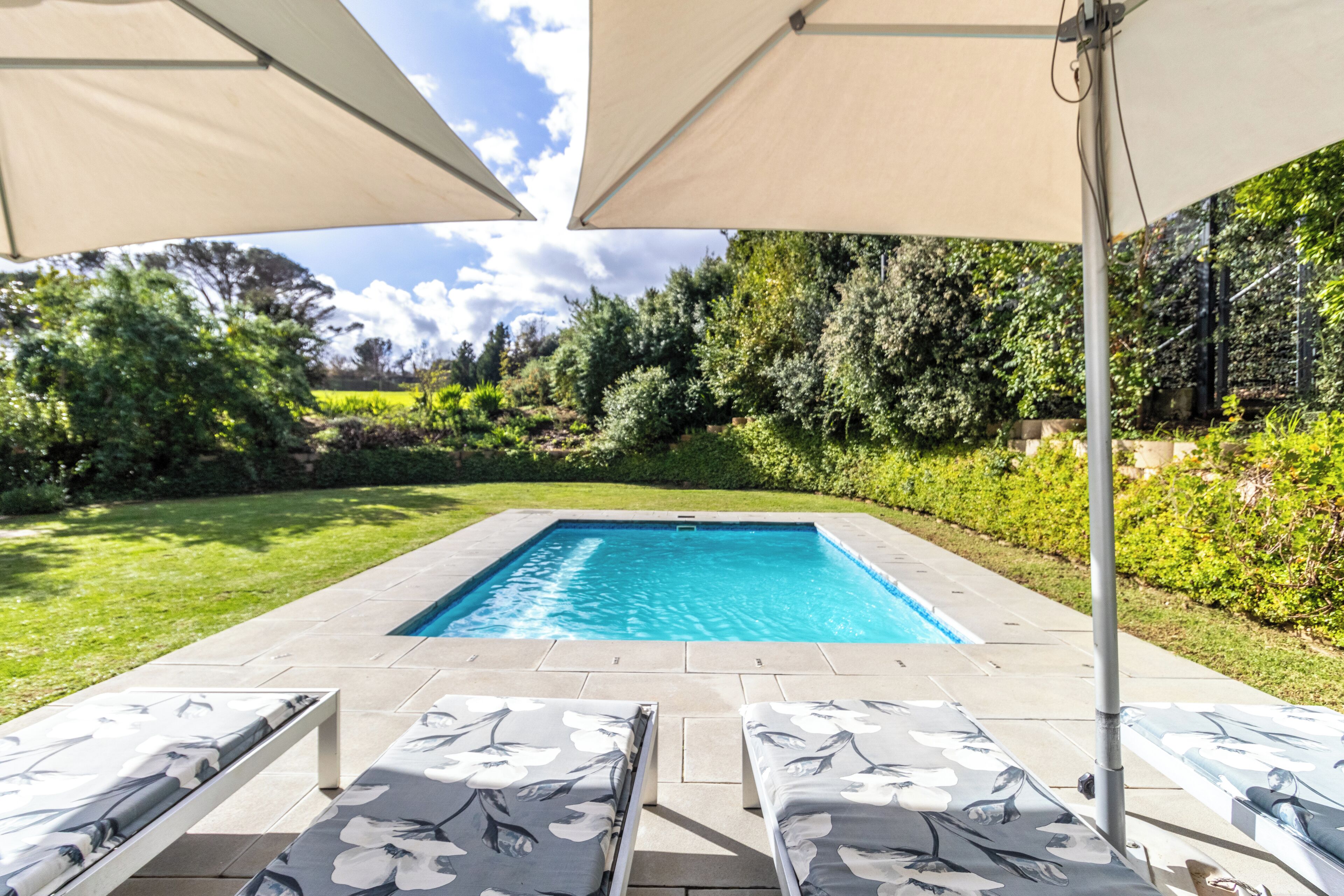 A rectangular pool with a tiled edge, surrounded by a patio with lounge chairs and umbrellas.