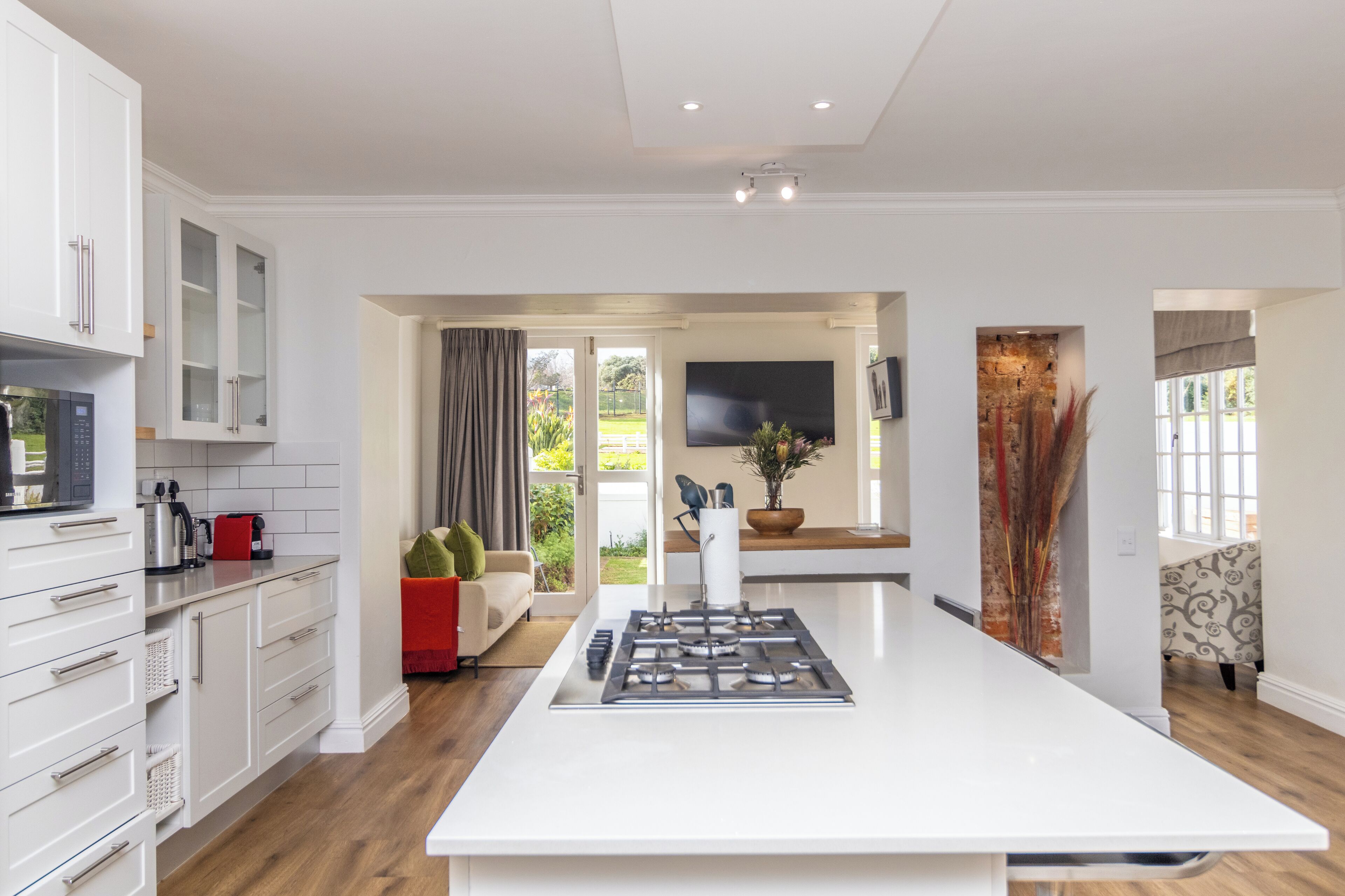 A modern kitchen with white cabinetry, a central island, and a flat-screen TV mounted on the wall.